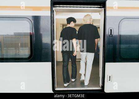 Deux jeunes hommes embarquent dans un train à grande vitesse moderne à Séoul, Corée du Sud - vue arrière à travers ouvert Banque D'Images