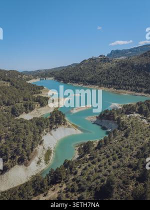 Vue aérienne du réservoir de Guadalest avec de l'eau turquoise entourée de forêts de pins et de collines escarpées sous un ciel bleu clair à Alicante, Valence Comm Banque D'Images