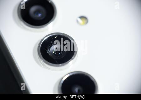 Photo macro d'un objectif d'appareil photo de smartphone fissuré et cassé sur un fond blanc avec mise au point sélective Banque D'Images