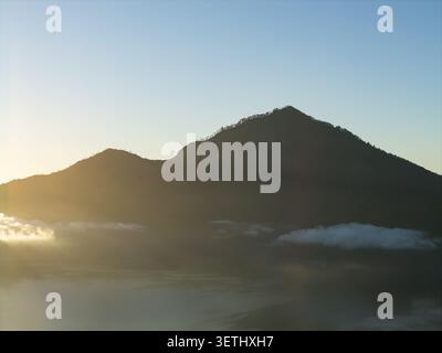Vue aérienne du lac Batur et du paysage volcanique environnant au lever du soleil avec une lumière dorée éclairant la brume au-dessus de l'eau à Kintamani, Bali, Banque D'Images