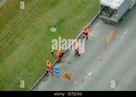 Travailleurs routiers remplaçant la bordure de béton sur la rue de la ville. Hommes en uniforme installant la bordure de trottoir. Équipe de travailleurs de la construction effectuant l'entretien des routes Ser Banque D'Images