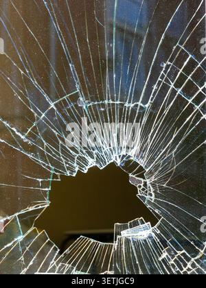Gros plan de verre brisé avec trou d'impact et fissures rayonnantes. Texture abstraite spectaculaire montrant des dommages, des fractures et de la fragilité Banque D'Images