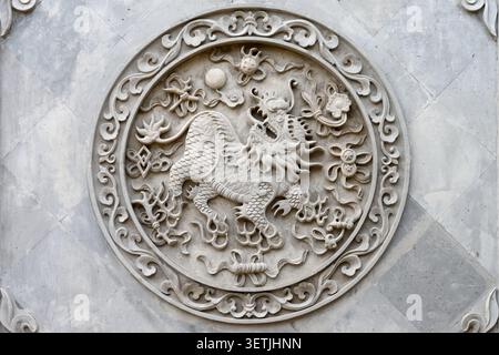 Sculpture en relief Qilin en pierre ornée dans un médaillon chinois circulaire sur le mur du temple Banque D'Images