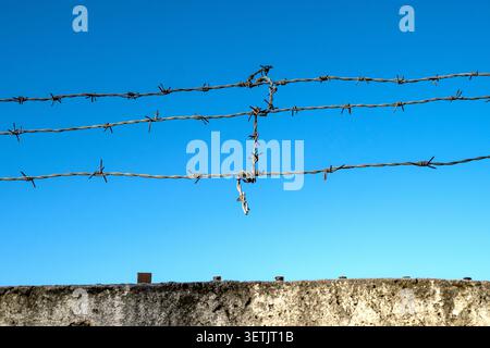 Fil de fer barbelé et mur de béton contre le ciel bleu, image conceptuelle Banque D'Images