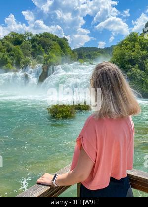 Vue arrière d'une femme admirant les puissantes cascades du parc national de Krka en Croatie entouré d'une végétation luxuriante. Cascades d'eau douce pittoresques avec pu Banque D'Images