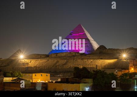 Al Gizeh, Gouvernorat de Gizeh, Égypte - 18 juin 2026 : vue de la Grande Pyramide de Gizeh illuminée de lumières violettes et bleues la nuit, face à un dar Banque D'Images