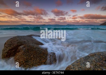 Vue sur Misery Beach avec des rochers de granit, des vagues douces se lavant sur le sable, et un ciel coloré de coucher de soleil sur l'océan Austral à Torndirrup, Weste Banque D'Images