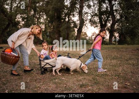 Mère et filles tirant des jumeaux et un chien dans un chariot, profitant d'une promenade tranquille dans le parc Banque D'Images