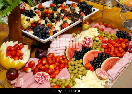 Table de pâturage gourmande avec fromage brie prosciutto salami raisins fraises et grenade artistiquement arrangés. Une préparation alimentaire visuellement attrayante Banque D'Images
