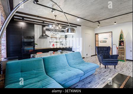 espace de vie contemporain avec une cuisine ouverte, avec un canapé sarcelle, des accents de bois sombre et un mélange d'éclairage industriel et élégant Banque D'Images