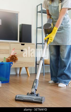 Photo recadrée d'une femme aspirant le plancher en bois avec un aspirateur sans fil Banque D'Images