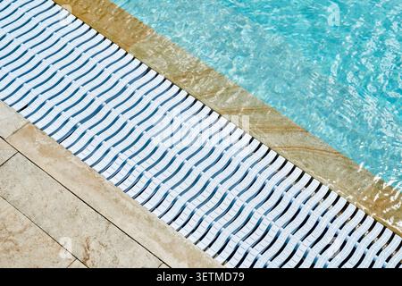 Le bord en marbre de la piscine avec une eau bleue cristalline et une grille de drainage en plastique blanc. Banque D'Images