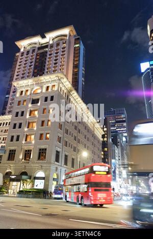 HONG KONG - 18 JUILLET 2023 : L'hôtel Peninsula illuminé la nuit par un bus à impériale rouge passant à Tsim Sha Tsui. Banque D'Images