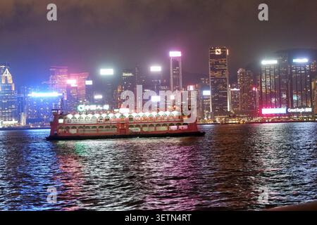 HONG KONG - 18 JUILLET 2023 : un bateau rose illuminé traverse le port Victoria devant les gratte-ciel nocturnes Banque D'Images