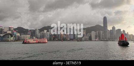 HONG KONG - 18 JUILLET 2023 : un bateau de croisière rose et une jonque à voile rouge traversent le port Victoria au crépuscule. Banque D'Images