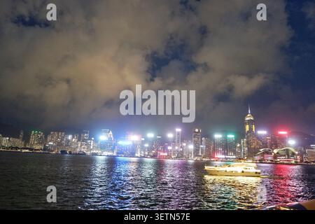 HONG KONG - 18 JUILLET 2023 : un yacht traverse le port Victoria sous les gratte-ciel illuminés de Central Plaza la nuit. Banque D'Images