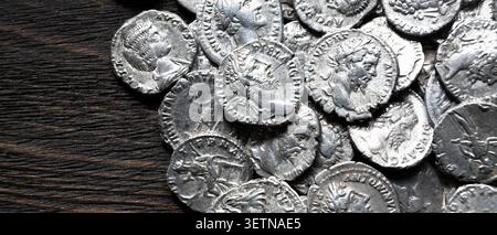 Gros plan, plan au-dessus du ciel, d'une collection de pièces d'argent anciennes dispersées sur une surface en bois sombre et texturée. Les pièces comportent un relief détaillé pr Banque D'Images