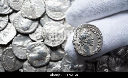 Une photographie en gros plan montrant une main portant un gant d'inspection en coton blanc tenant une pièce d'argent ancienne. La pièce dispose d'un port de profil détaillé Banque D'Images
