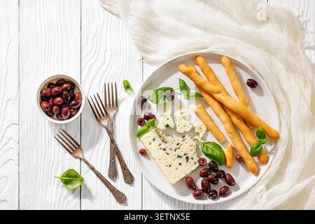 Assiette d'apéritif italienne Gorgonzola con grissini e olive avec fromage bleu, gressins croustillants et feuilles de basilic frais sur assiette blanche sur bois blanc Banque D'Images