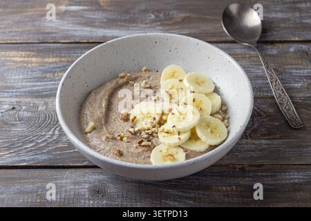 Bouillie de lin saine garnie de tranches de banane, de noix hachées et de graines dans un bol en céramique. Petit déjeuner nutritif avec des ingrédients naturels, copie Banque D'Images