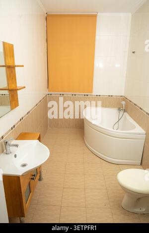 Intérieur de salle de bains spacieux et bien éclairé présentant une baignoire d'angle blanche avec des luminaires chromés, meuble-lavabo en bois élégant avec évier blanc intégré, Banque D'Images