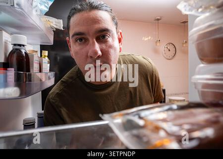 Homme regardant à l'intérieur d'un réfrigérateur ouvert à la recherche de quelque chose à manger tard dans la nuit Banque D'Images