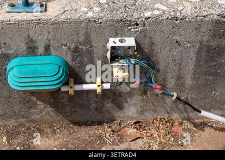 Vue rapprochée d'une boîte de jonction électrique extérieure avec des fils exposés et un capteur sarcelle fixé à un mur en béton Banque D'Images