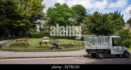 Un jardinier tendant à des parterres de fleurs dans un parc public avec un véhicule utilitaire garé sur le bord de la route à proximité de Bath UK Banque D'Images