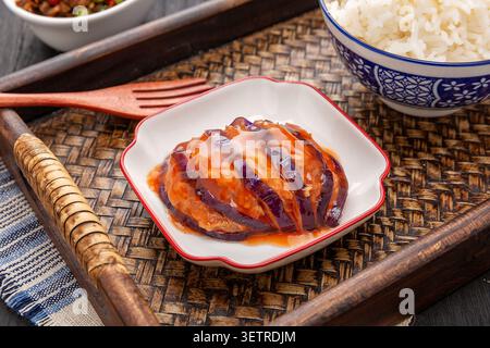 Gros plan d'une seule portion d'aubergine chinoise farcie de lanterne avec sauce salée, servie sur une assiette carrée vintage avec du riz cuit à la vapeur sur un tra de bambou Banque D'Images