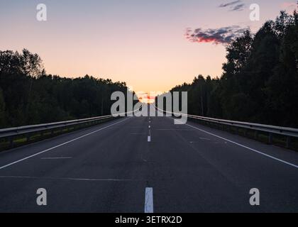 Vue sur le coucher du soleil sur une autoroute tranquille entourée d'arbres luxuriants dans la soirée Banque D'Images