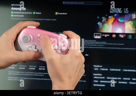 New York, États-Unis - 18 mai 2026 : jouer Among US jeu PC avec manette de jeu dans la main gros plan vue sur fond d'écran Banque D'Images