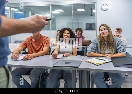 Groupe diversifié de jeunes étudiants assis à des bureaux, écoutant attentivement un professeur dans une salle de classe moderne d'université ou de collège, engagés dans l'apprentissage Banque D'Images