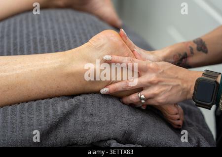 Personne recevant un massage thérapeutique professionnel des pieds sur une serviette sombre Banque D'Images