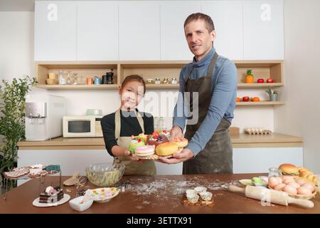 Père multiracial et fille tenant un plateau de pâtisseries colorées dans la cuisine pour la fête des pères Banque D'Images
