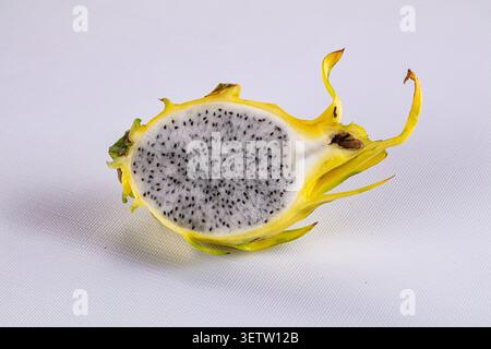 Gros plan de fruits de dragon jaune coupés en deux montrant une chair blanche parsemée de graines noires. La peau jaune vif contraste avec la surface blanche propre. S souple Banque D'Images