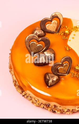 Un gros plan moyen d'un gâteau artisanal au caramel, mettant en valeur les gouttes de glaçage brillant impeccable, la croûte de noix texturée et les cœurs de chocolat détaillés de Banque D'Images