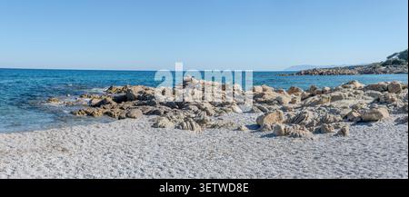 Paysage panoramique avec des rochers de granit sur la plage blanche et skerries dans l'eau bleue à la crique sur la rive de la mer Méditerranée, tourné dans la lumière printanière lumineuse a Banque D'Images