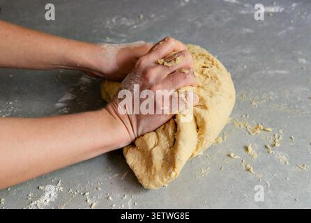 Mains de boulanger façonnant une boule de pâte à pâte brisée. Gros plan des mains d'une personne pétrissant et formant une boule solide de pâte crue maison sur un gris Banque D'Images