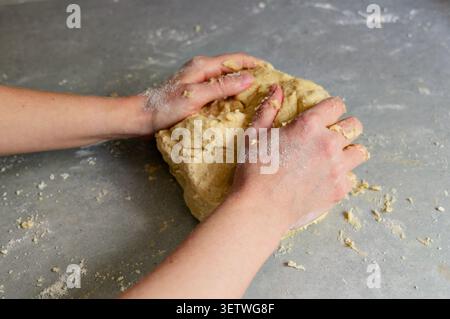 Mains de boulanger façonnant une boule de pâte à pâte brisée. Gros plan des mains d'une personne pétrissant et formant une boule solide de pâte crue maison sur un gris Banque D'Images