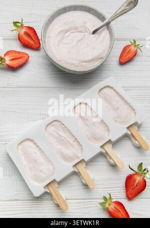 Popsicles au yaourt aux fraises dans un moule avec des baies fraîches et du yaourt crémeux sur une table en bois Banque D'Images