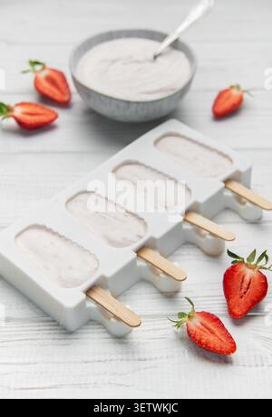 Popsicles au yaourt aux fraises dans un moule avec des baies fraîches et du yaourt crémeux sur une table en bois Banque D'Images