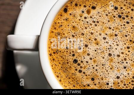 Vue de dessus macro de la crème espresso au café frais avec bulles. Mousse de café espresso aromatique dans une tasse en céramique blanche. Texture de bulles dorées pour café mar Banque D'Images
