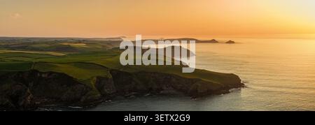 Vue aérienne d'un promontoire côtier accidenté baigné par la lumière dorée du coucher du soleil, avec des falaises superposées s'étendant au loin. Banque D'Images
