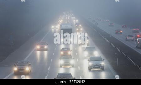 Voitures et camions se déplaçant sur une autoroute avec des phares allumés dans un épais brouillard Banque D'Images