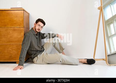 Un jeune homme avec une barbe dans des lunettes montre un look tendance et décontracté dans un espace studio Banque D'Images