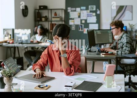 Femme noire couvrant le visage tout en travaillant dans le bureau stressant Banque D'Images