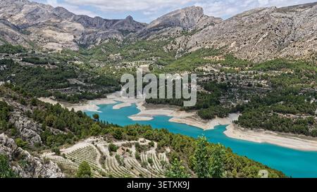Réservoir de Guadalest en espagne montrant des niveaux d'eau bas, des montagnes et des forêts de pins sous ciel nuageux Banque D'Images