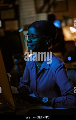 Femme adulte noire travaillant sur un ordinateur portable pendant le service de soirée Banque D'Images