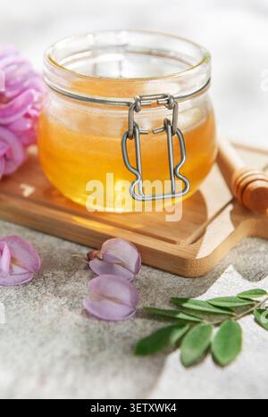Miel dans un bocal en verre avec des fleurs d'acacia rose et une benne en bois sur une planche Banque D'Images