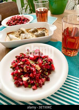 Un bol contient une salade faite de betteraves bouillies, pommes de terre, carottes, avocats et petits pois. Le merlu blanc cuit repose dans un plat à côté de la salade. Un verre assis Banque D'Images